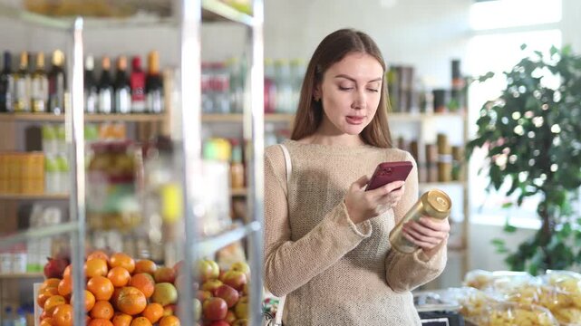 Young woman customer at shop scans QR code on beer can package using phone camera . High quality 4k footage
