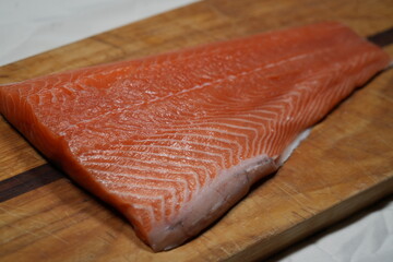 A filet of raw atlantic salmon on a wooden cutting board. © scott