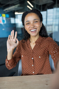 Video call and remote work communication, happy woman waving hand during online meeting on laptop at office desk for professional business connection