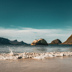 Panoramic view of gentle ocean wave splashing on sandy beach with solitary rock and majestic mountains under blue sky in Norway © Quality by Simon