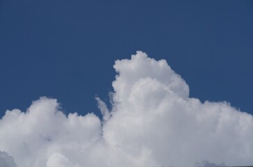 A large fluffy white cumulus cloud rising dramatically against a clear deep blue sky, creating a striking natural weather background with soft texture and bright contrast. © johnandpenny