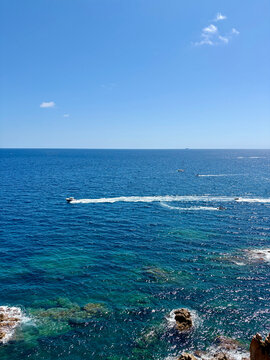 A jet ski leaving a white wake trail across the blue mediterranean sea with clear sky