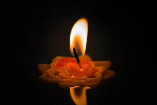 Close up of small decorative candle burning brightly against dark background warm glowing flame melted wax creating peaceful atmosphere