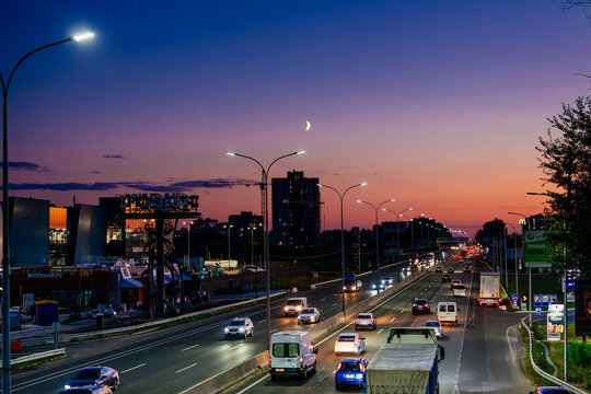 Chabany, Ukraine - September 16, 2026: Evening traffic on the illuminated Odesa highway heading south towards Odesa during dusk. A beautiful sunset sky with a crescent moon is visible over the road.