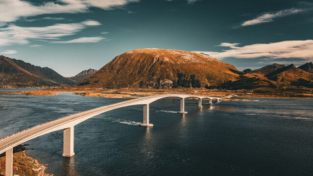 Modern concrete road bridge curving across ocean fjord towards a mountain in scenic northern Norway landscape