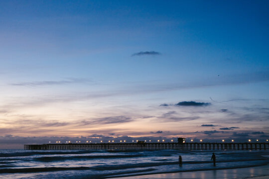Silhouettes on the beach with an illuminated pier at twilight