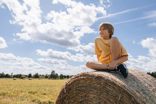 Young boy sitting on a hay bale in a summer field