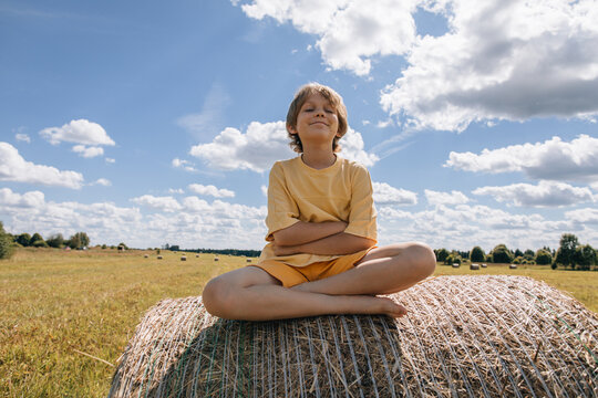 Happy young boy enjoying a sunny day on a hay bale