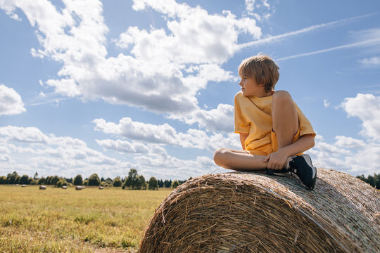 Blond boy sitting on a hay bale in a sunny field