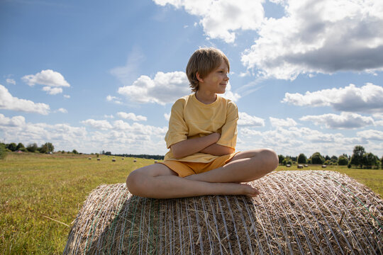 Smiling boy sits cross legged on a round hay bale