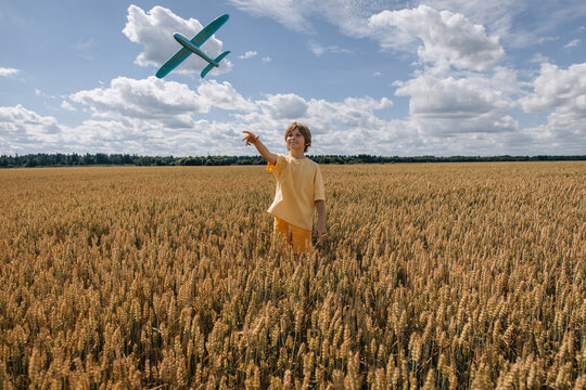 Boy with toy plane in a vast golden wheat field