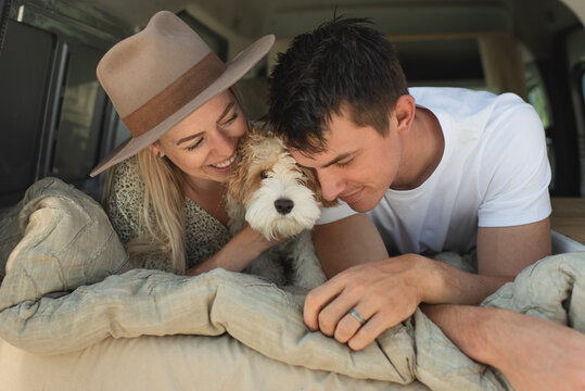 Young couple cuddling with puppy in campervan bed on road trip