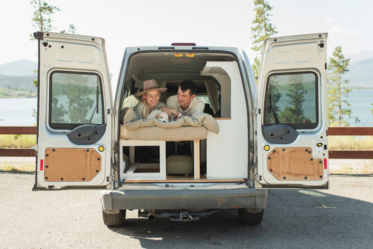 Couple and puppy relaxing in camper van by mountain lake on weekend