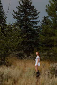 Woman with long red hair looks back in a forest clearing