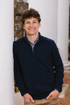 Happy college student leaning against a white pillar