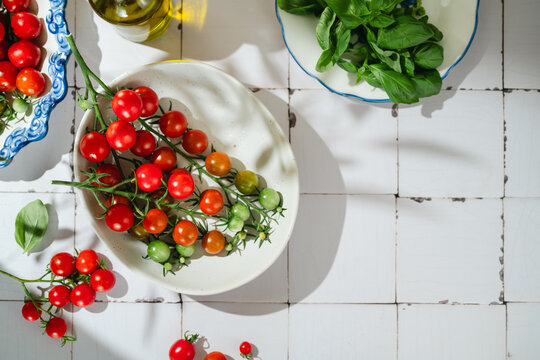 Fresh cherry tomatoes and basil in bowls on a white tiled surface