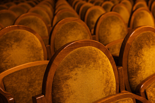 Empty golden brown velvet theater seats in rows inside dark concert hall auditorium background
