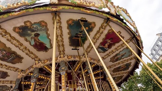 Vintage carousel spinning in paris with ornate painted ceiling panels and gold columns.