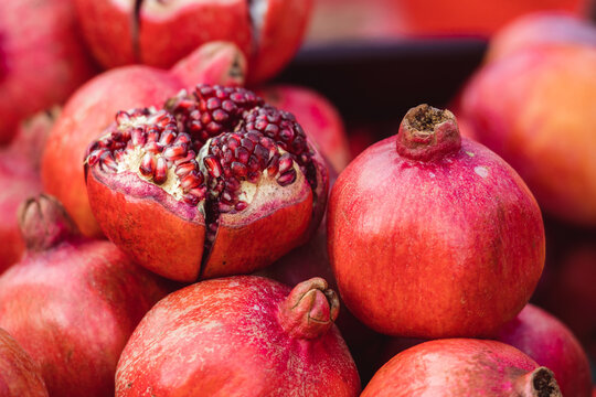 Fresh pomegranates characterized by their typical reddish skin and an open fruit revealing the distinctive internal arils, in a fruit and vegetables market