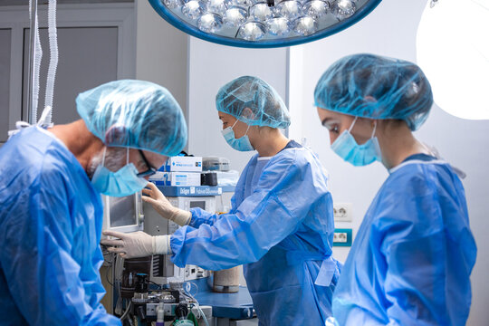 Surgeon operating medical equipment. Team of doctors wearing scrubs and surgical masks in hospital operating room, Healthcare and medicine concept, Professional medical staff working during surgery.