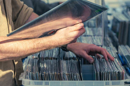 Man browsing vinyl records in crates at a flea market. Close-up of hands flipping through vintage LP albums