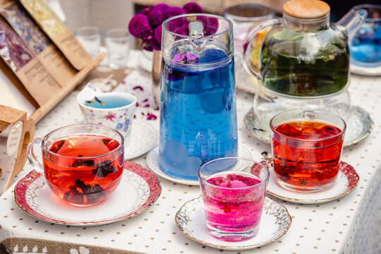 Glass teapot and cups with different kinds of herbal tea on the table in a street food market