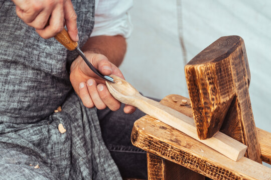 Close-up of a craftsman carving a wooden spoon by hand using traditional woodworking tools. Artisan in apron working with wood, shavings visible. Concept of craftsmanship, handmade