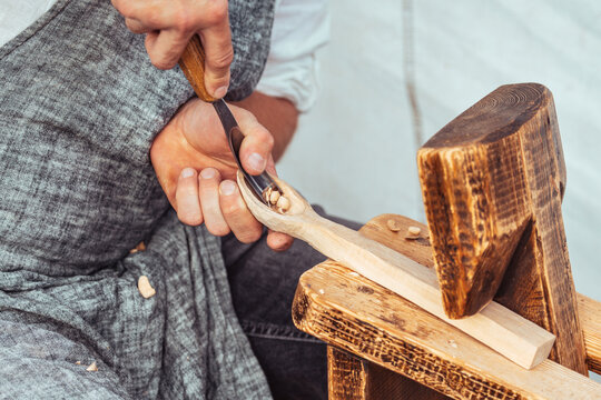 Close-up of a craftsman carving a wooden spoon by hand using traditional woodworking tools. Artisan in apron working with wood, shavings visible. Concept of craftsmanship, handmade
