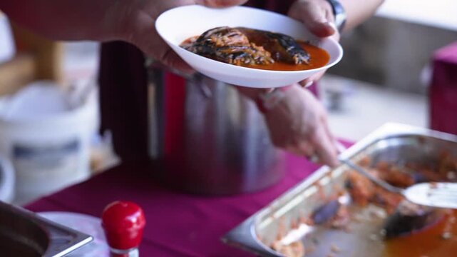 Cook ladling hot hal&aacute;szl&eacute;, a spicy fisherman's soup with paprika, into a bowl for a guest