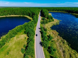 Obraz premium Aerial view of winding roadway bordered by lush green trees and serene blue lakes