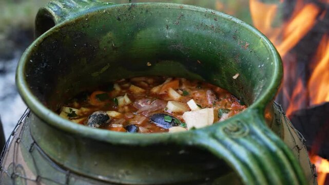 Delicious rustic goulash cooking in a ceramic pot over an open campfire at a festival