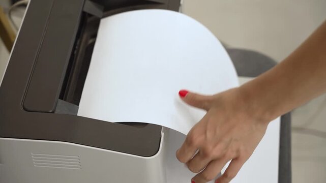 Close-up of a laser printer printing a document and a woman's hand taking the paper sheet