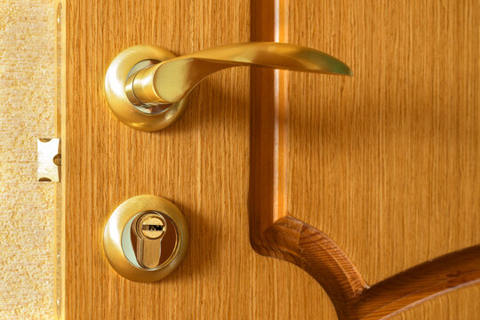 Close-up of gold curved handle and round key lock on natural wooden interior door. Concepts of home security, protection, privacy, access control, door hardware, residential safety, locksmith services