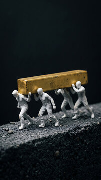 Miniature white human figurines working together to lift and carry a heavy golden metal block piece
