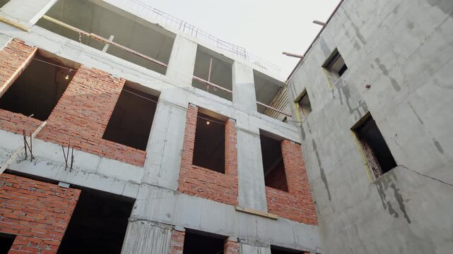 Unfinished brick and concrete walls rise around open inner courtyard. Construction exposes structural frame and empty window openings
