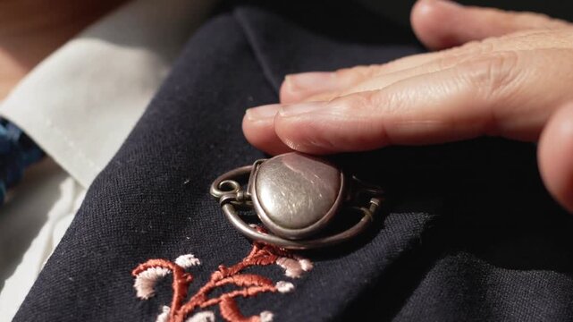 Hovering hand moving down, adjusting and rubbing brooch at lapel, showing navy blazer and blue tie