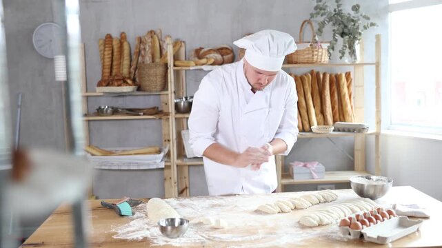 Professional baker in white uniform and cap cutting raw dough with knife to make croissants or buns 