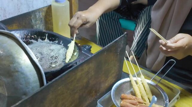 A street food vendor carefully fries egg rolls in hot oil, creating a crispy golden texture while preparing this popular savory snack.