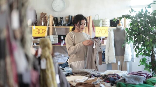 In sales area of store, Latin woman customer chooses trousers. Creating capsule wardrobe, branded clothing at affordable prices. Modern urban fashion, casual practical clothes 