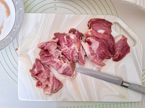 Fresh raw pork meat sliced with knife on white artificial stone cutting board next to ceramic plate and board stand high angle view. Cooking preparation, butchery process, and kitchenware concept.