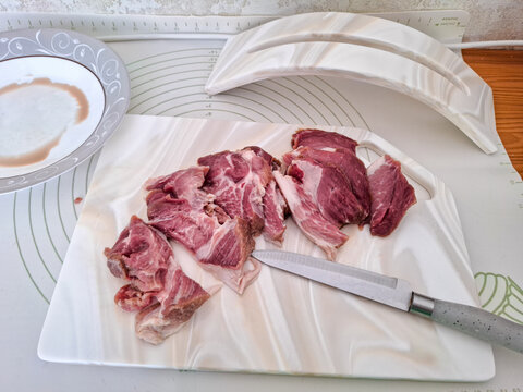 Fresh raw pork meat sliced with knife on white artificial stone cutting board next to ceramic plate and board stand high angle view. Cooking preparation, butchery process, and kitchenware concept.