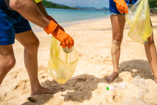 Close up of two volunteers collect plastic bottles and trash on sandy beach.