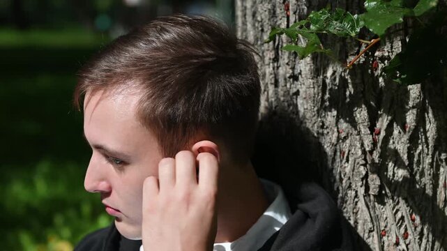 Man putting wireless earbuds in his ears, enjoying new device. Sitting on the park, he inserted earbuds and let the soothing melodies wash over her. 4K footage