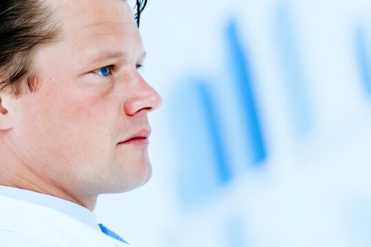 Side profile of fair skinned adult man with blue eyes and damp hair against softly blurred blue and white background in close up portrait