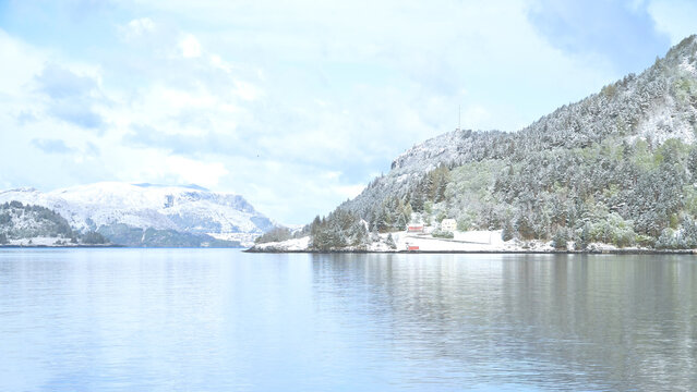 Quiet Fjord Landscape with Snow-Covered Mountains and Red Cabin.
