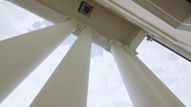 Tall slender columns rise toward bright cloud-streaked sky. Row of tall architectural columns extend vertically toward clear blue sky