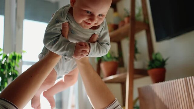 Caring father enjoying a playful moment with his cheerful baby son, lifting him up high in his arms in their sunlit home, fostering a heartwarming connection and cherished childhood experiences