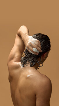 Man applying shampoo foam to wet hair from elevated rear view. Concept of hair hygiene, scalp cleansing and washing routine.