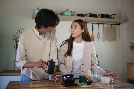 Young Asian couple pouring water and preparing matcha tea at home.