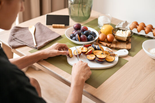 Person cut plums on halves, preparing ingredients for sweet fruit cake cooking